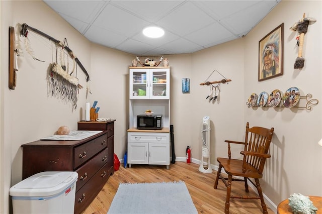 sitting room featuring baseboards, a drop ceiling, and light wood-type flooring