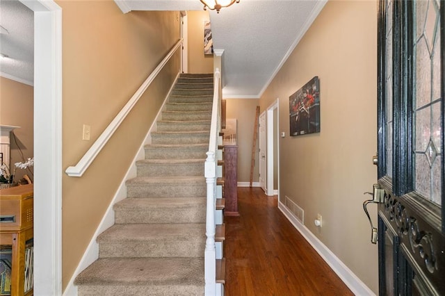 staircase with visible vents, ornamental molding, a textured ceiling, and wood finished floors