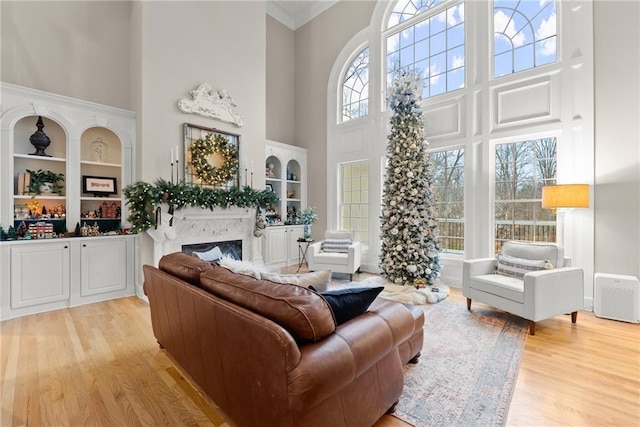 living room with built in shelves, a fireplace, light hardwood / wood-style floors, and a high ceiling