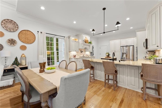 dining space with a notable chandelier, ornamental molding, sink, and light hardwood / wood-style flooring