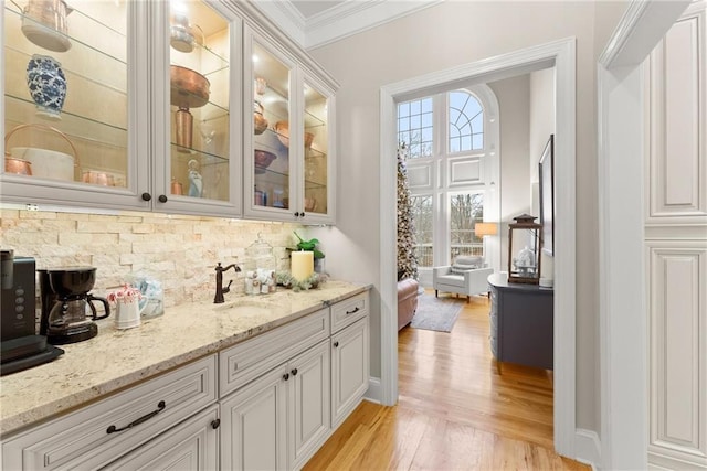 bar featuring light stone counters, a healthy amount of sunlight, sink, light hardwood / wood-style floors, and white cabinetry