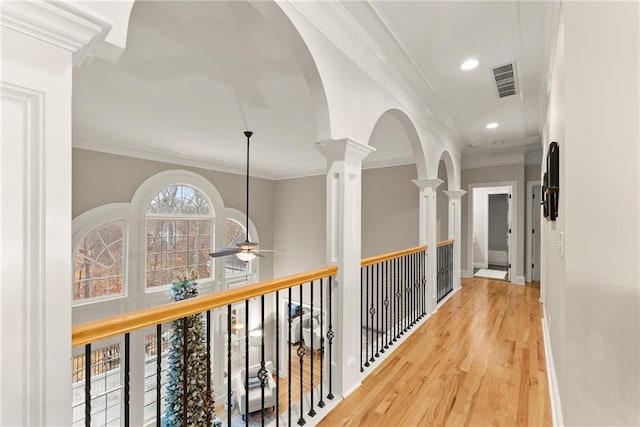 hall with ornate columns, wood-type flooring, and ornamental molding