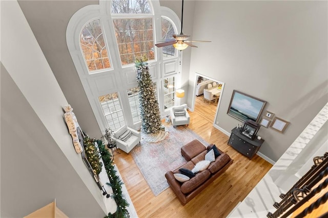 living room featuring ceiling fan, a towering ceiling, and wood-type flooring