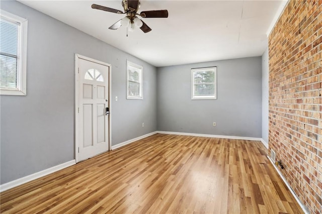 foyer with light wood-type flooring, ceiling fan, and brick wall