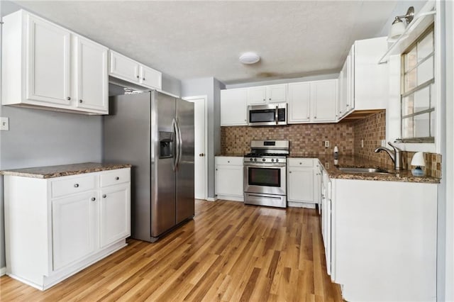 kitchen with dark stone counters, stainless steel appliances, sink, light hardwood / wood-style floors, and white cabinetry