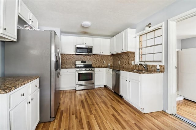 kitchen with light hardwood / wood-style floors, white cabinetry, dark stone counters, and appliances with stainless steel finishes