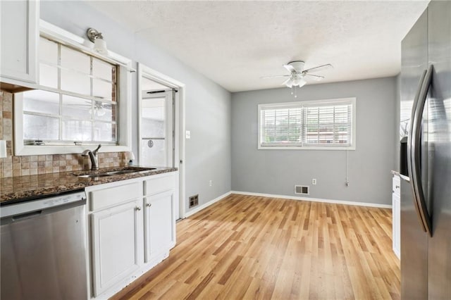 kitchen with dark stone counters, sink, light hardwood / wood-style floors, white cabinetry, and stainless steel appliances