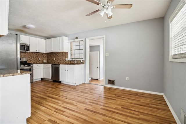 kitchen featuring white cabinets, appliances with stainless steel finishes, light wood-type flooring, and tasteful backsplash