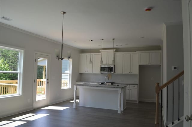 kitchen featuring dark hardwood / wood-style flooring, white cabinetry, decorative light fixtures, light stone counters, and a center island with sink