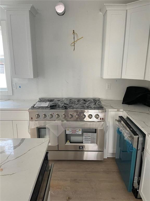 kitchen with dishwasher, light stone counters, double oven range, white cabinets, and hardwood / wood-style flooring