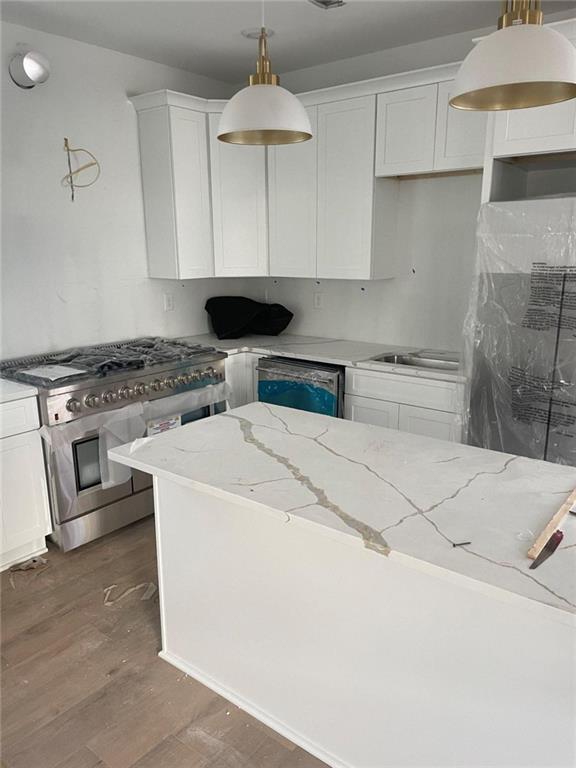 kitchen featuring white cabinetry, light stone countertops, hanging light fixtures, dark hardwood / wood-style flooring, and appliances with stainless steel finishes