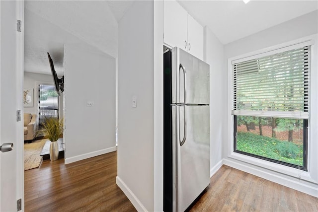 kitchen with stainless steel fridge, hardwood / wood-style flooring, and white cabinetry