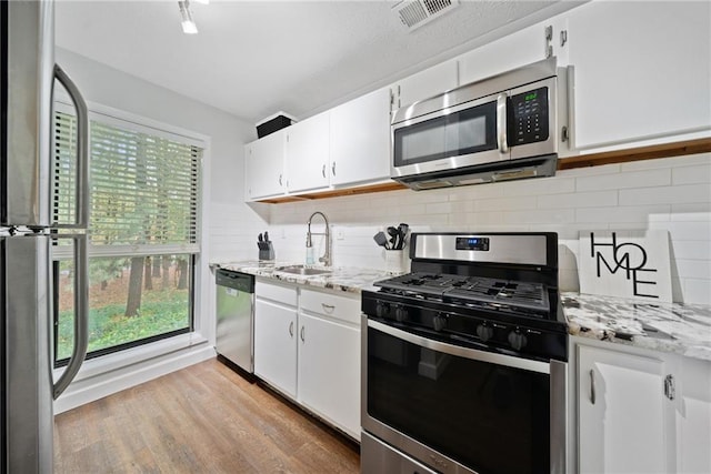 kitchen with stainless steel appliances, white cabinetry, light hardwood / wood-style floors, and sink