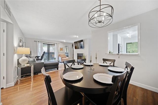 dining space featuring a fireplace, wood-type flooring, and an inviting chandelier