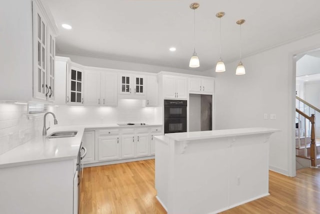 kitchen with light wood-type flooring, pendant lighting, sink, white cabinets, and double oven