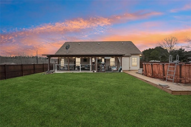 back house at dusk with a patio area and a lawn