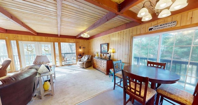 dining area with carpet floors, wood walls, a chandelier, and beamed ceiling