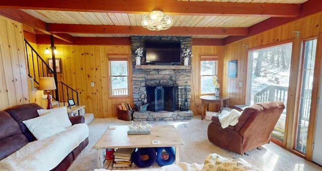 carpeted living area with stairway, a wealth of natural light, wood walls, and a stone fireplace