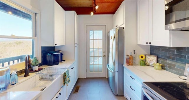 kitchen featuring light tile patterned floors, decorative backsplash, appliances with stainless steel finishes, white cabinetry, and wooden ceiling