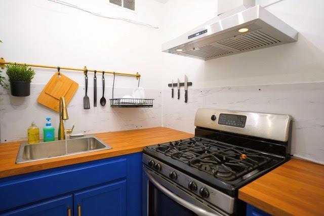 kitchen with blue cabinetry, stainless steel range with gas cooktop, sink, and ventilation hood