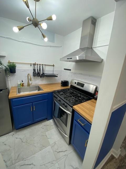 kitchen with wooden counters, sink, stainless steel appliances, and wall chimney range hood