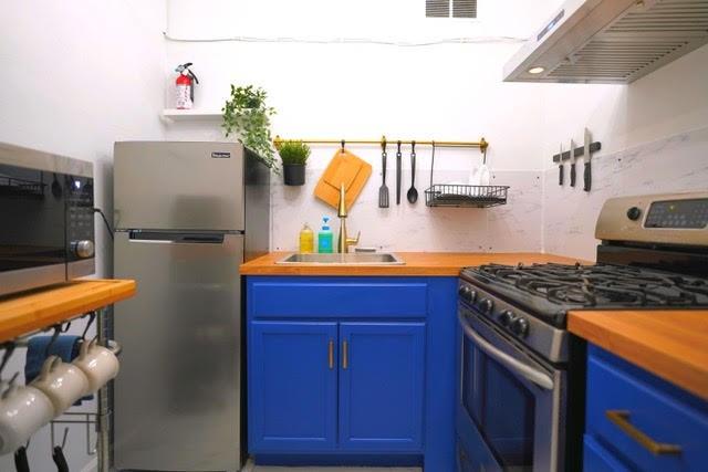 kitchen featuring stainless steel appliances, butcher block countertops, blue cabinets, and range hood