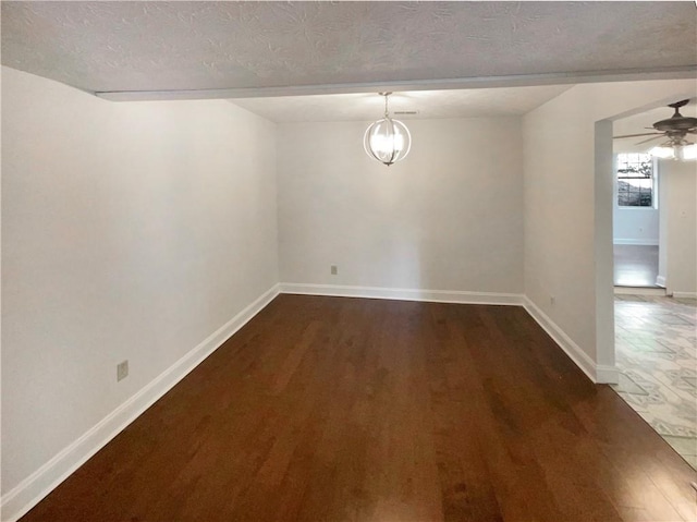 spare room featuring ceiling fan with notable chandelier, dark wood-type flooring, and a textured ceiling