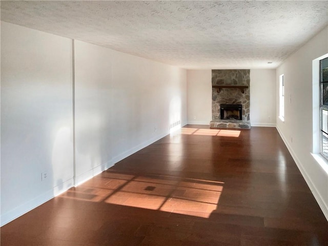 unfurnished living room featuring a stone fireplace, dark hardwood / wood-style flooring, and a textured ceiling