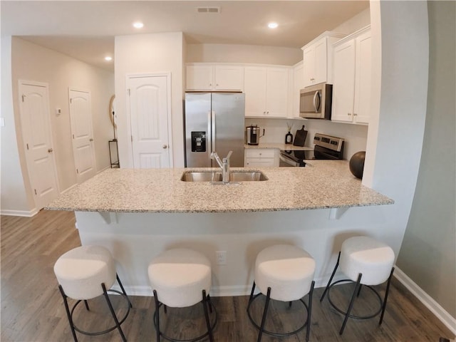 kitchen with appliances with stainless steel finishes, light stone countertops, white cabinets, sink, and kitchen peninsula