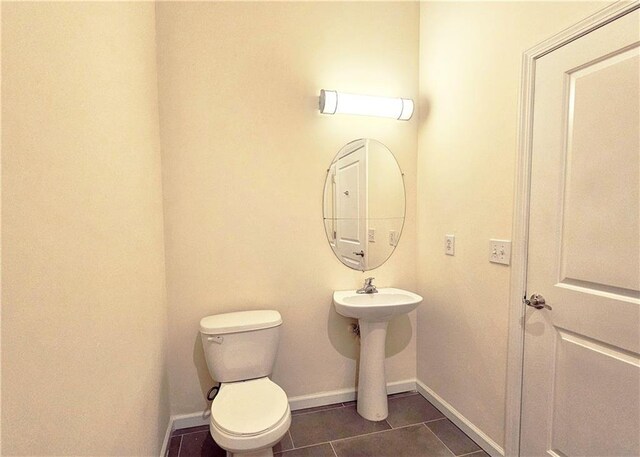half bathroom featuring baseboards, toilet, tile patterned flooring, and a sink