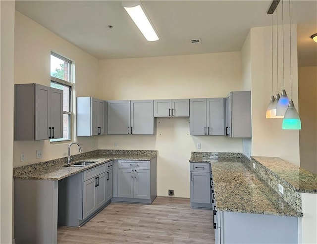 kitchen with stone countertops, gray cabinetry, a sink, and light wood-style floors