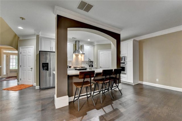 2515 Gadsen Walk, Duluth, GA 30097 - kitchen featuring stainless steel appliances, arched walkways, wall chimney exhaust hood, dark wood finished floors, and crown molding