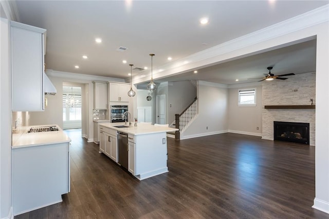 kitchen featuring a fireplace, decorative light fixtures, white cabinetry, an island with sink, and sink