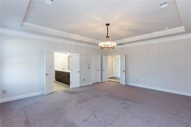 carpeted spare room with a raised ceiling, ornamental molding, and a chandelier