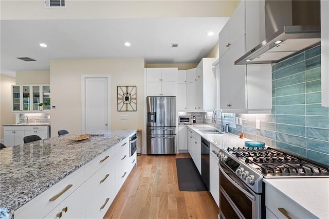 kitchen featuring white cabinets, wall chimney range hood, sink, light wood-type flooring, and appliances with stainless steel finishes