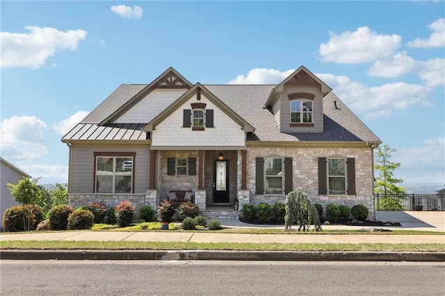 craftsman house featuring a standing seam roof, fence, a porch, and stone siding