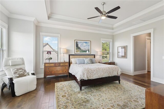 bedroom with dark wood-style flooring, a tray ceiling, multiple windows, and ornamental molding