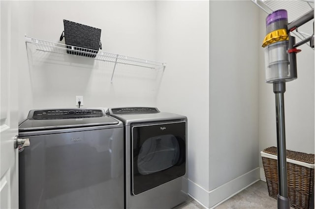 clothes washing area featuring light tile patterned floors, laundry area, washing machine and dryer, and baseboards