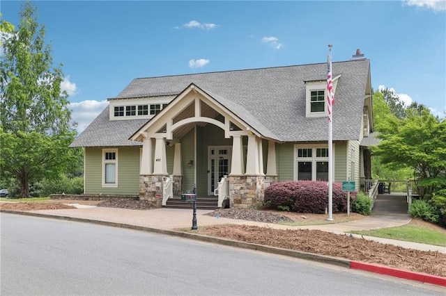 craftsman house with a porch, roof with shingles, and stone siding