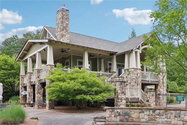 rear view of house featuring roof with shingles, stairs, stone siding, a chimney, and a ceiling fan