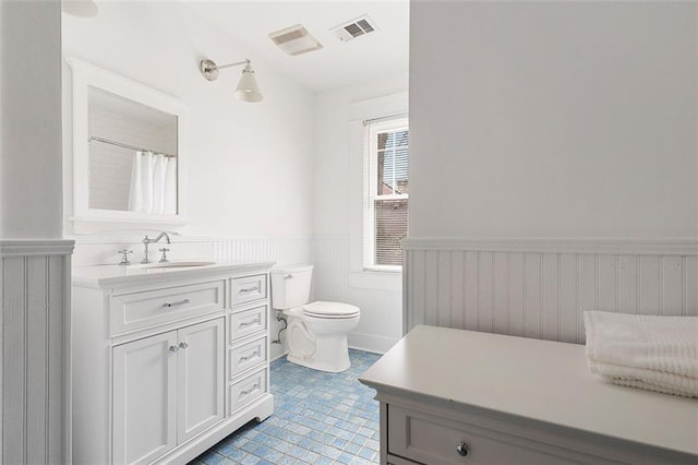 full bath featuring toilet, vanity, visible vents, and wainscoting