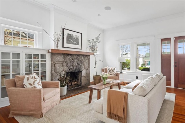 living area featuring a stone fireplace, ornamental molding, and wood finished floors