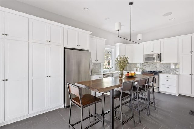 kitchen with tasteful backsplash, white cabinets, hanging light fixtures, stainless steel appliances, and light countertops