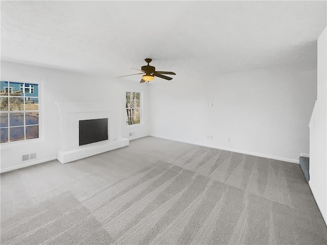 unfurnished living room featuring visible vents, a fireplace with raised hearth, baseboards, carpet flooring, and a ceiling fan