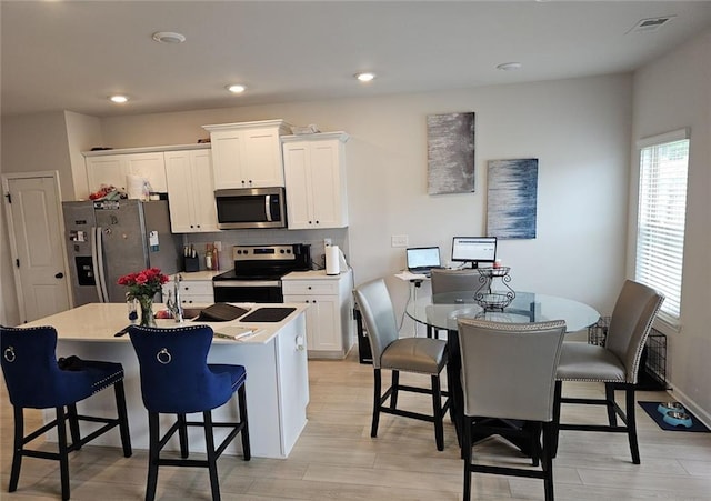 kitchen featuring white cabinetry, a center island with sink, a breakfast bar, and appliances with stainless steel finishes