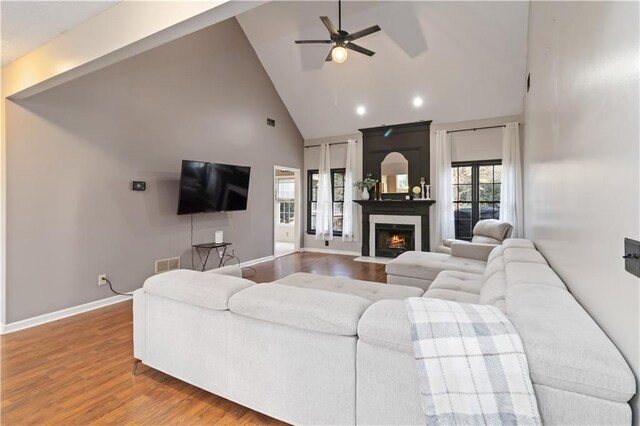 living room featuring hardwood / wood-style floors, a large fireplace, high vaulted ceiling, and ceiling fan