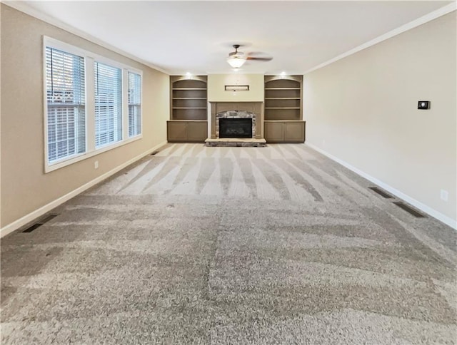 unfurnished living room with carpet flooring, a stone fireplace, built in features, and ornamental molding