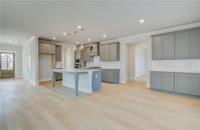 kitchen featuring an island with sink, custom range hood, light countertops, gray cabinetry, and pendant lighting