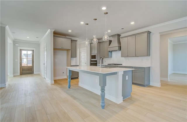 kitchen with a center island with sink, light countertops, premium range hood, pendant lighting, and a sink