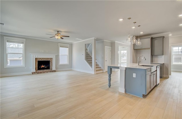 kitchen with an island with sink, open floor plan, light countertops, pendant lighting, and a sink